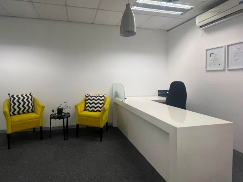 A professional office space featuring a built-in reception desk, suspended ceiling with recessed lighting, and a wall-mounted air conditioning unit.