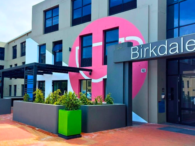 Front exterior view of the Birkdale 1 office building featuring modern architectural design, large windows, a metal pergola, and integrated planters.