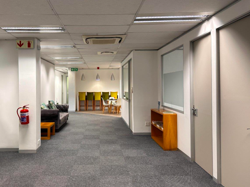 A well-maintained office corridor featuring carpeted flooring, suspended ceilings with recessed lighting, integrated air conditioning, and glass partitions for a professional workspace environment.