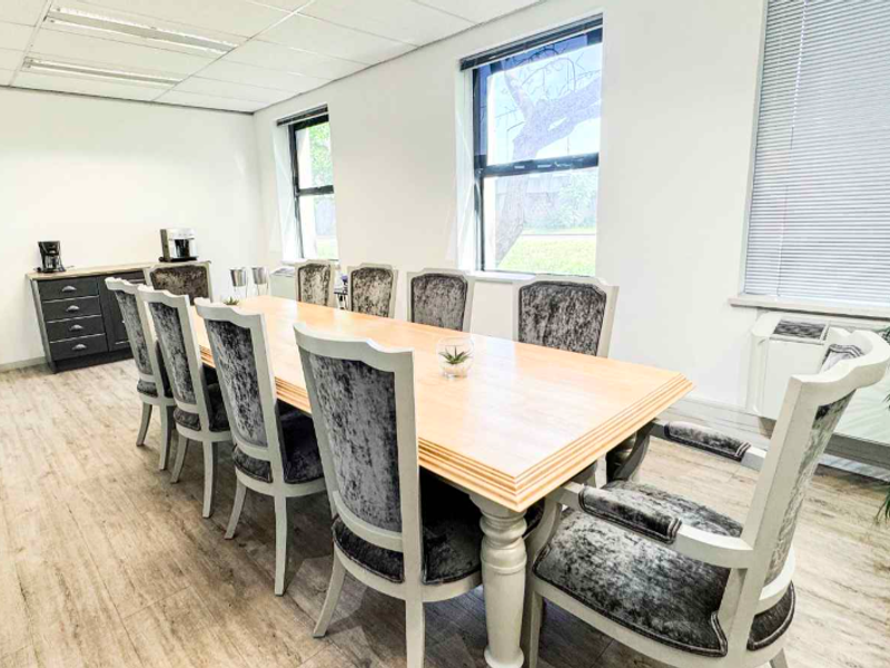 A professional office meeting room featuring laminate flooring, suspended ceiling, and large windows with blinds, providing a bright and functional workspace.