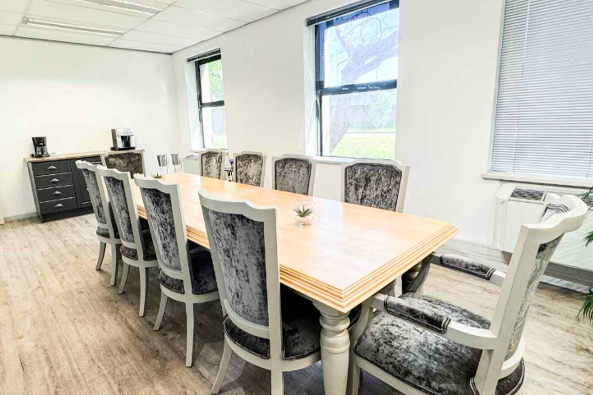 A professional office meeting room featuring laminate flooring, suspended ceiling, and large windows with blinds, providing a bright and functional workspace.