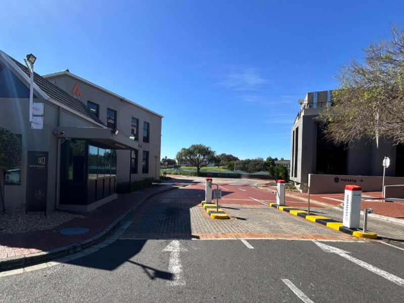 Entrance view of the office park featuring a security boom gate, paved driveway, and professional guard booth facility.