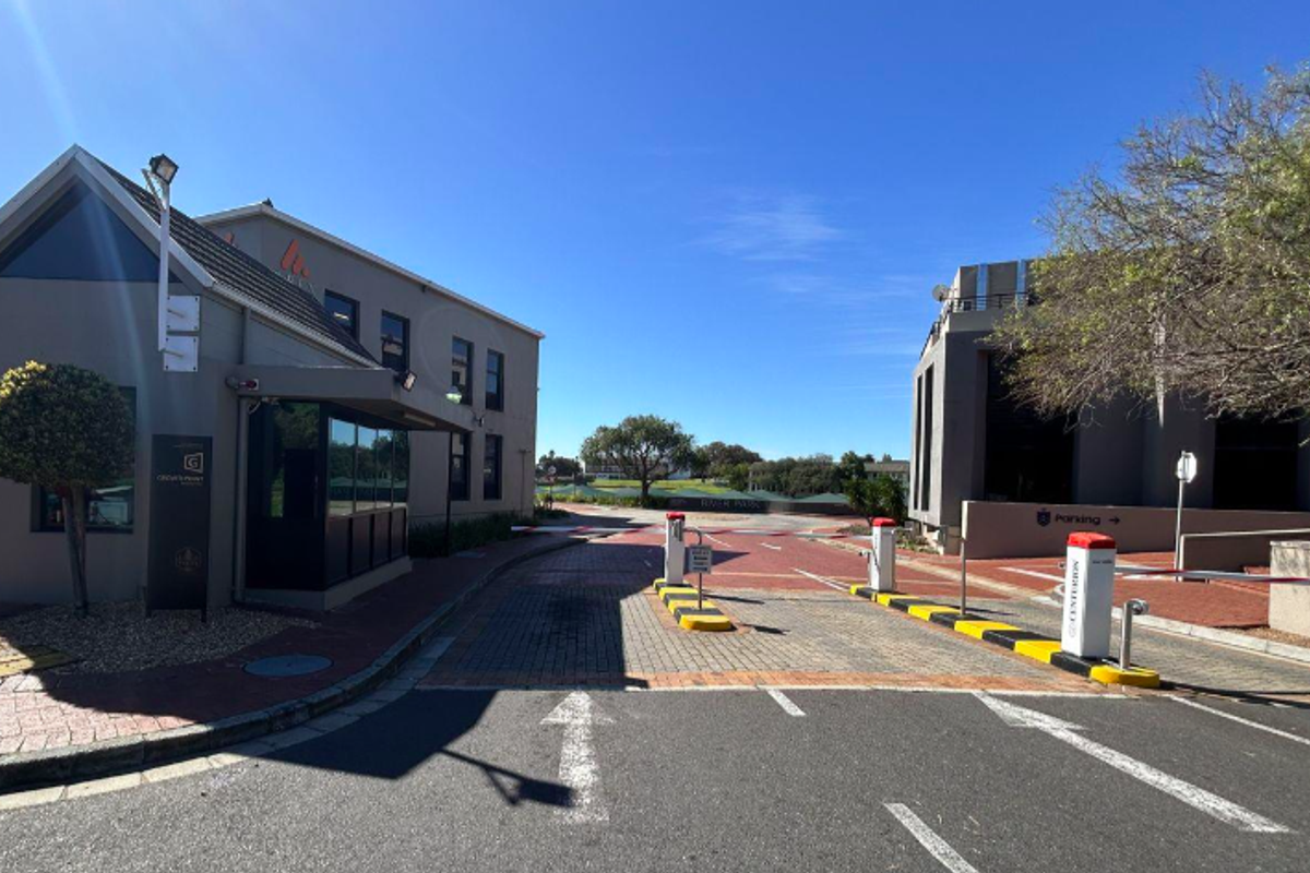 Entrance view of the office park featuring a security boom gate, paved driveway, and professional guard booth facility.