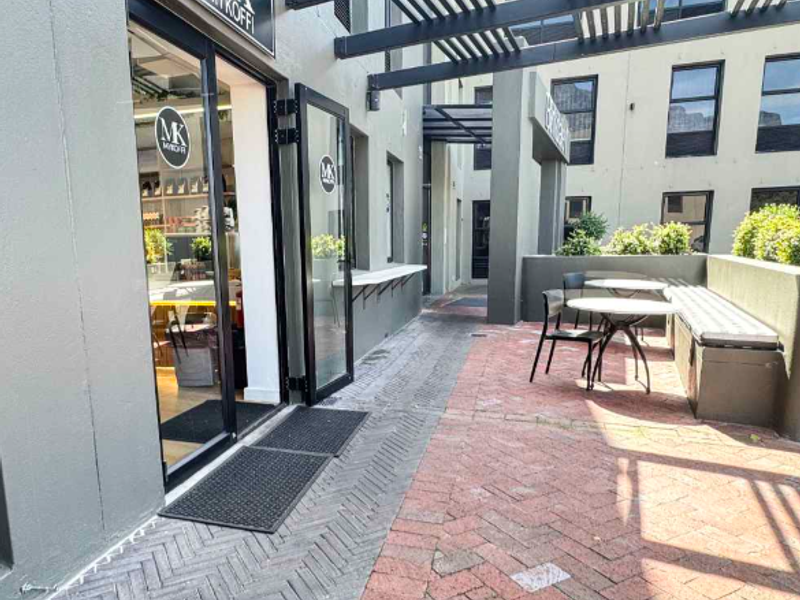 A well-maintained outdoor patio area featuring brick paving, a pergola structure, and a built-in bench, providing an inviting entrance to the office space.