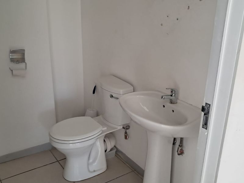 A compact bathroom featuring a pedestal basin and toilet with tiled flooring, requiring minor cosmetic updates to the wall surfaces.