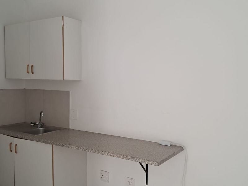 A compact kitchenette featuring basic base and wall-mounted cabinetry, a stainless steel sink, and a laminate countertop with a tiled splashback.