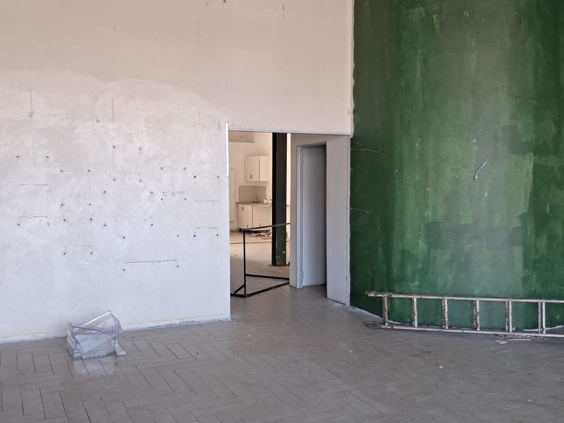 An empty industrial open-plan space featuring parquet flooring and a prominent green feature wall, requiring cosmetic refurbishment and wall repairs.