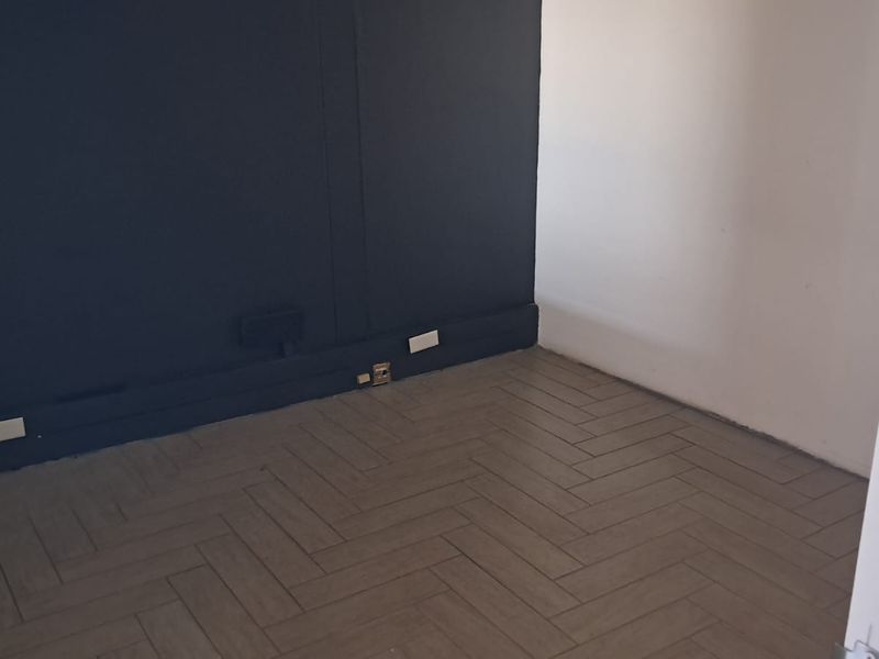 An empty office space featuring herringbone tile flooring and a dark accent wall with visible electrical infrastructure.