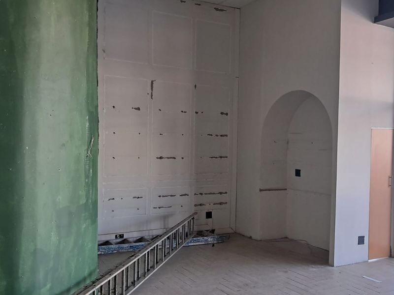 An unfinished interior space featuring an arched wall niche, large glass window, and visible wall surface damage requiring repair and finishing.