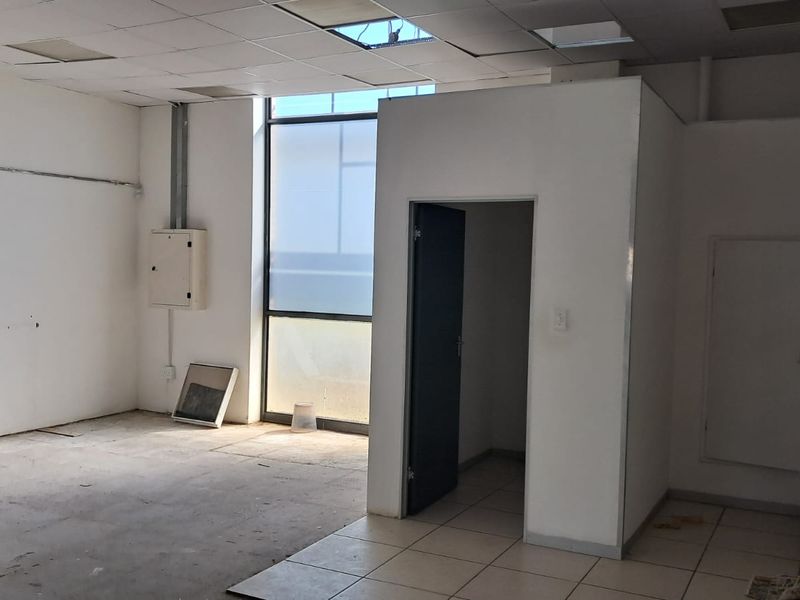 Open-plan industrial space featuring a kitchenette, tiled flooring, and a suspended ceiling with some maintenance required.