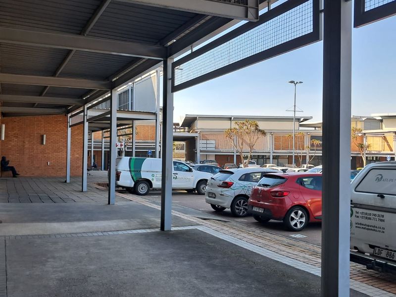 Exterior view of an industrial property featuring a covered walkway, brick facade, and an adjacent paved parking area.