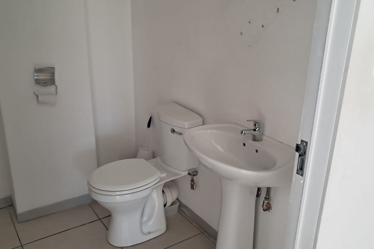 A compact bathroom featuring a pedestal basin and toilet with tiled flooring, requiring minor cosmetic updates to the wall surfaces.