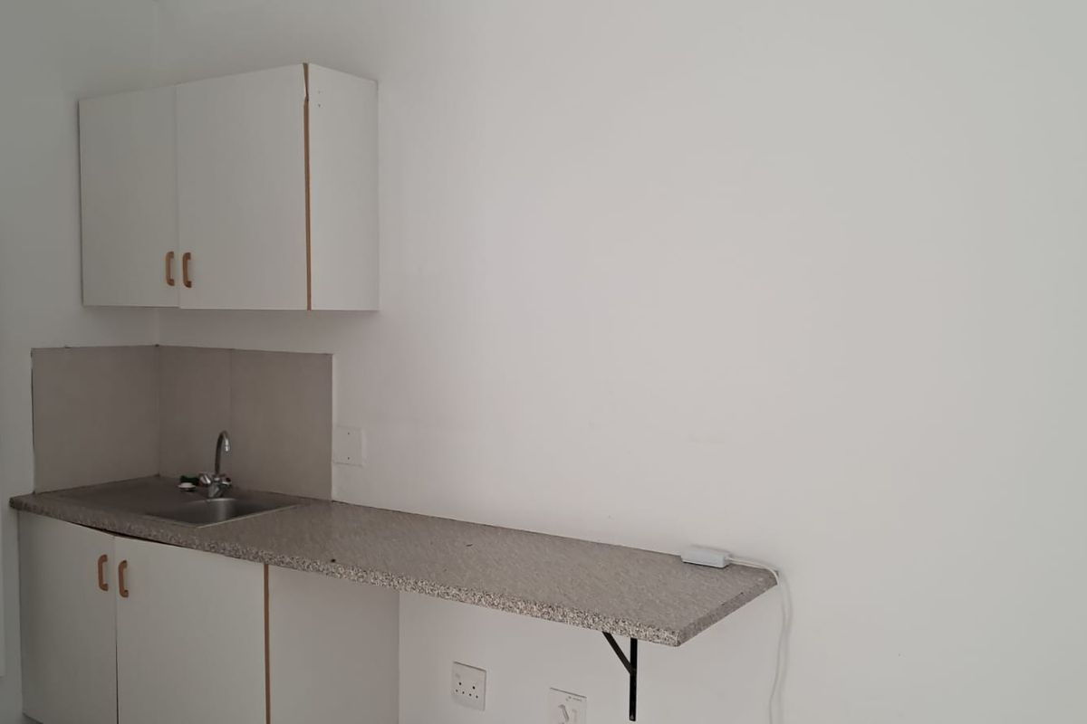 A compact kitchenette featuring basic base and wall-mounted cabinetry, a stainless steel sink, and a laminate countertop with a tiled splashback.