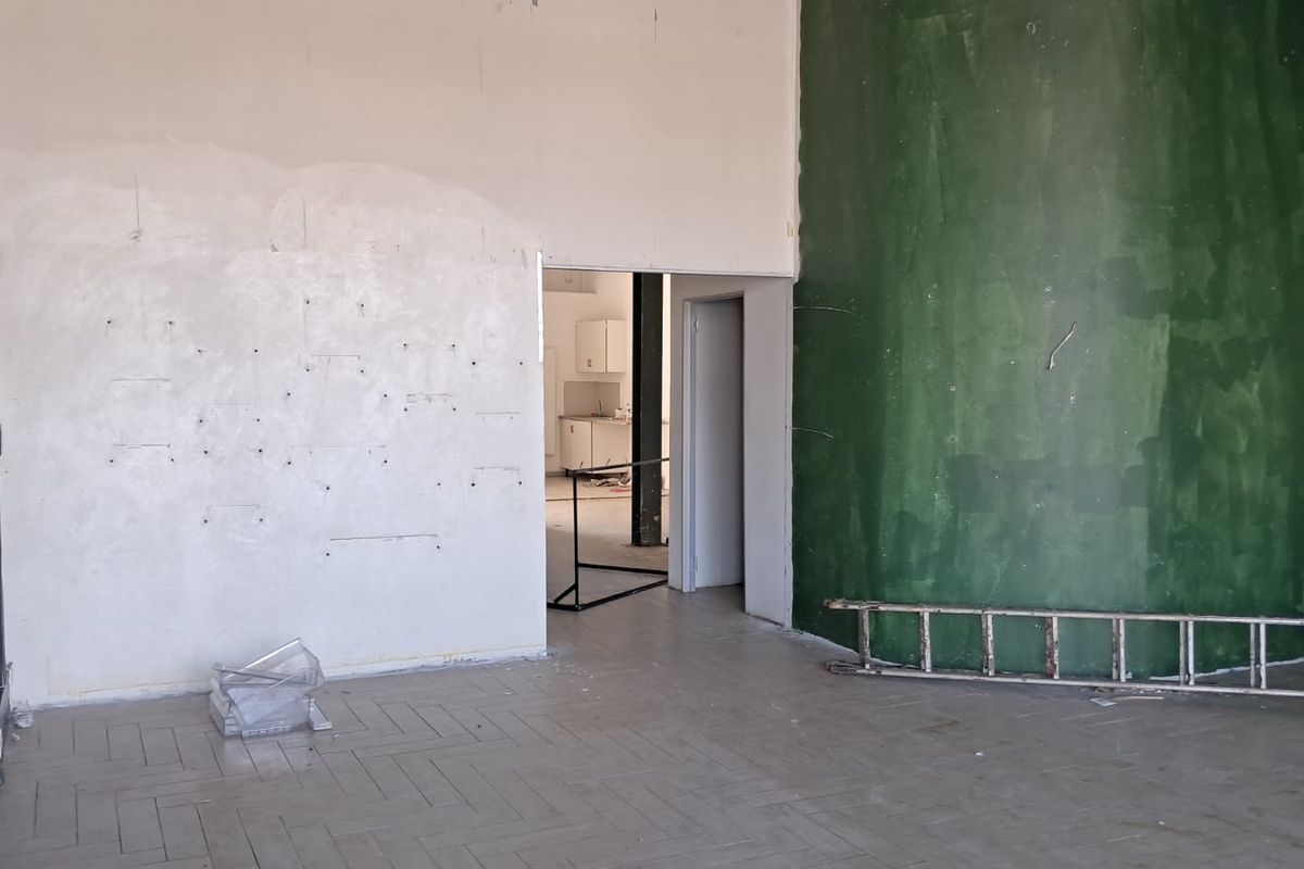 An empty industrial open-plan space featuring parquet flooring and a prominent green feature wall, requiring cosmetic refurbishment and wall repairs.