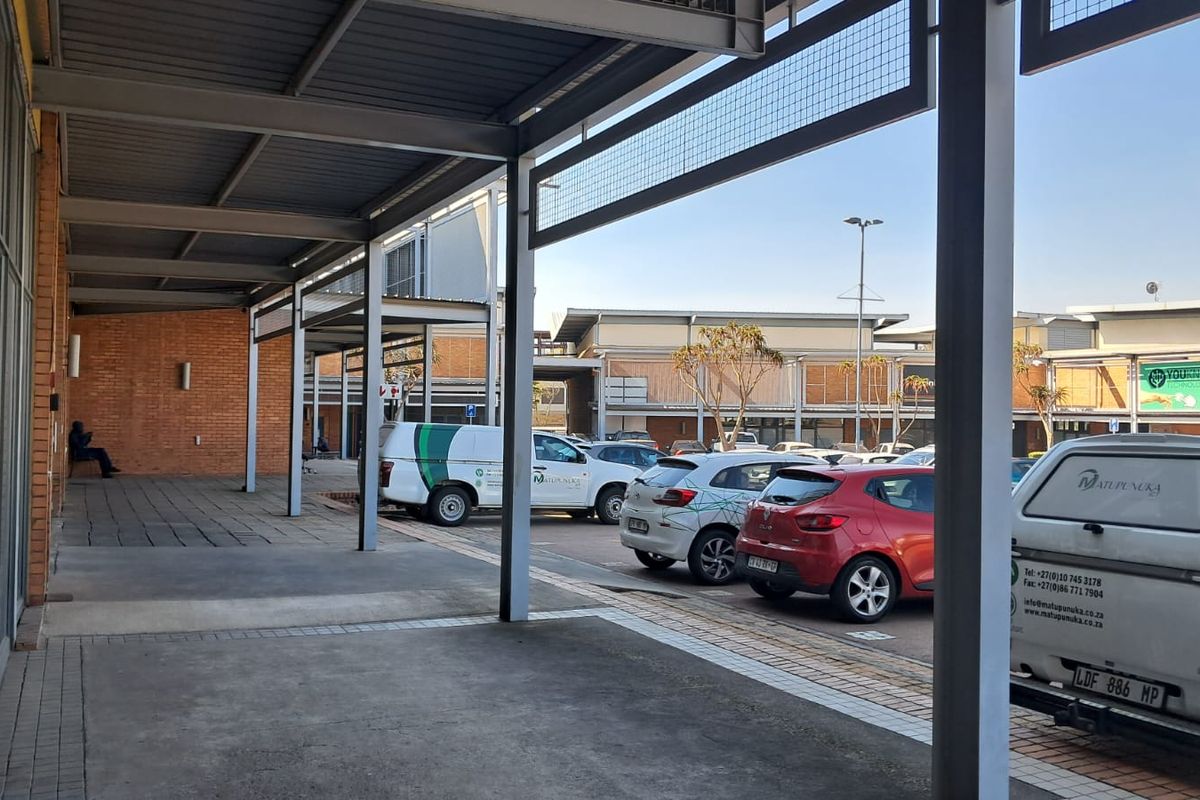 Exterior view of an industrial property featuring a covered walkway, brick facade, and an adjacent paved parking area.