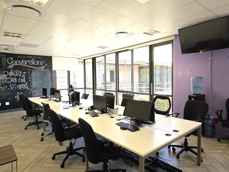 A functional open-plan office space featuring herringbone flooring, a large chalkboard wall, and ample natural light through floor-to-ceiling windows.
