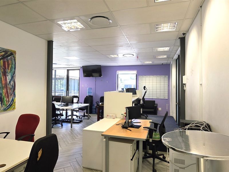 Open-plan office space featuring a mix of herringbone tile and carpet flooring, suspended ceilings with recessed lighting, and a functional layout.