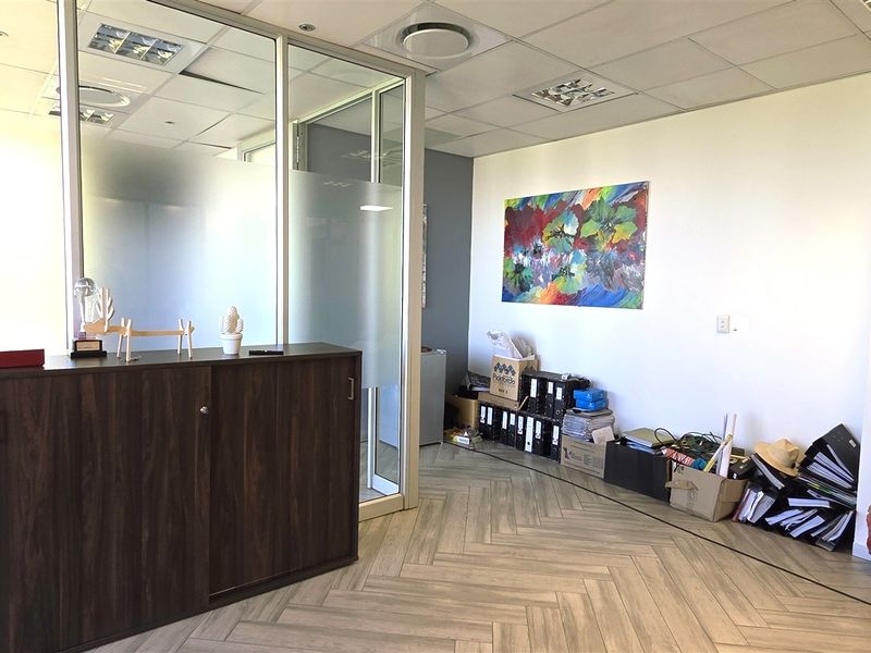 Modern office space featuring a glass partition wall, herringbone flooring, and recessed ceiling lighting, providing a professional and bright work environment.