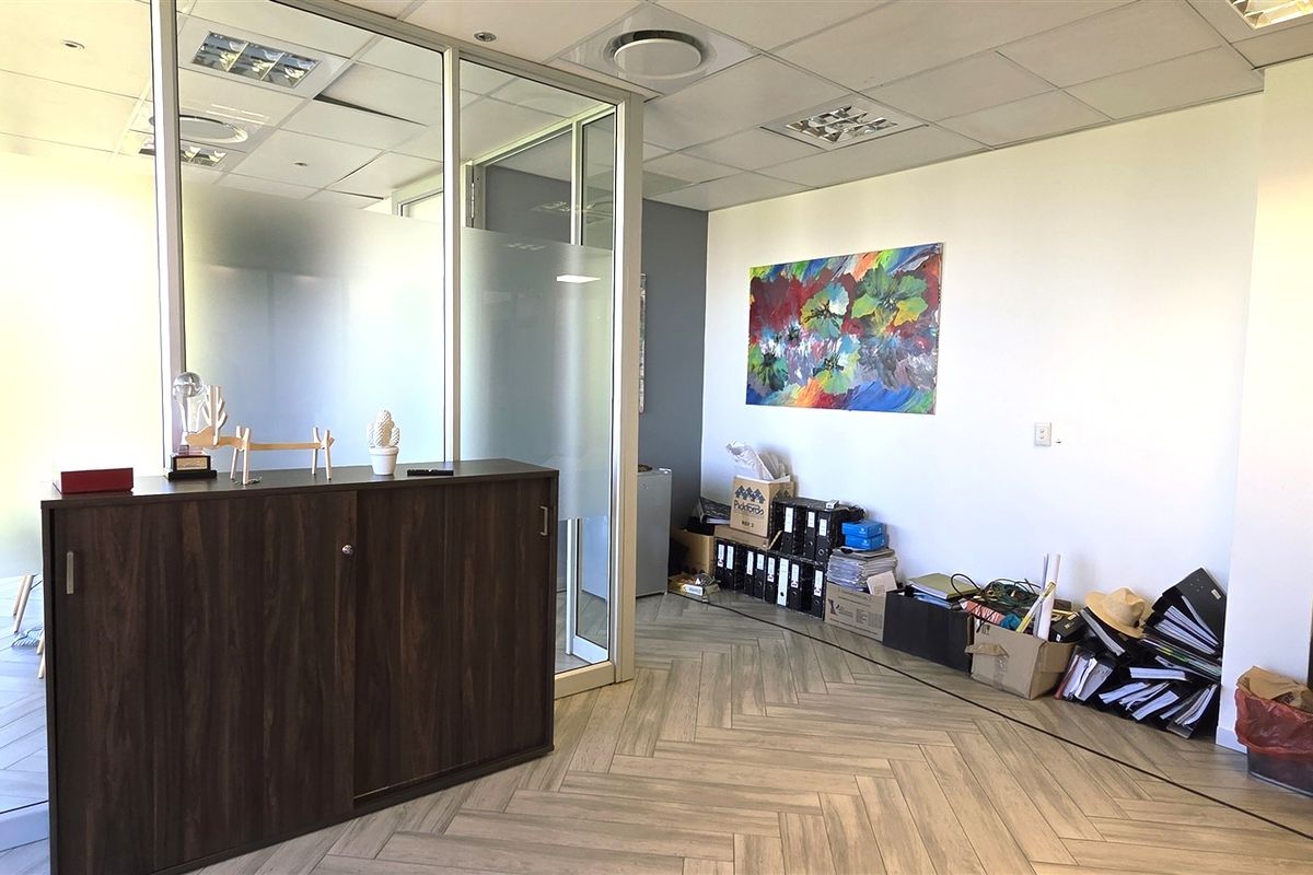 Modern office space featuring a glass partition wall, herringbone flooring, and recessed ceiling lighting, providing a professional and bright work environment.