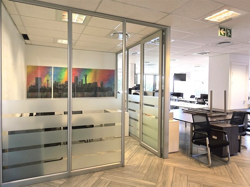 Modern office space featuring glass partitioning, suspended ceilings with recessed lighting, and durable herringbone flooring in a professional open-plan layout.