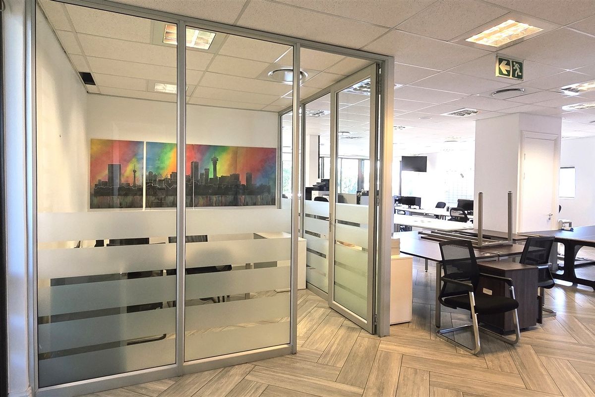Modern office space featuring glass partitioning, suspended ceilings with recessed lighting, and durable herringbone flooring in a professional open-plan layout.