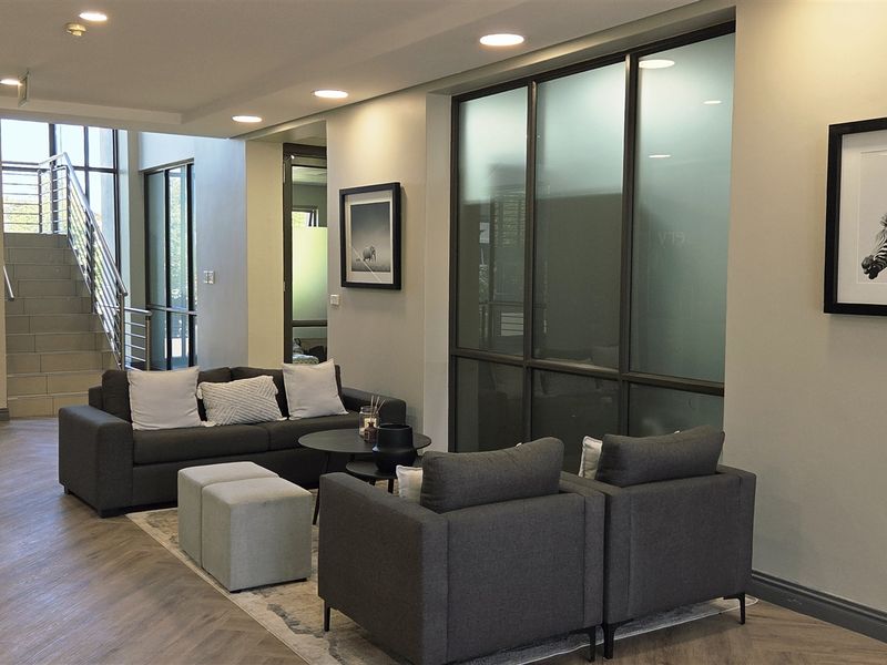 Modern office reception area featuring herringbone flooring, recessed lighting, and glass-partitioned office spaces with a staircase leading to upper levels.