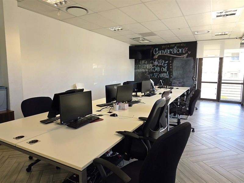 A bright, modern office space featuring large windows, tiled flooring, a suspended ceiling with recessed lighting, and a dedicated chalkboard wall.