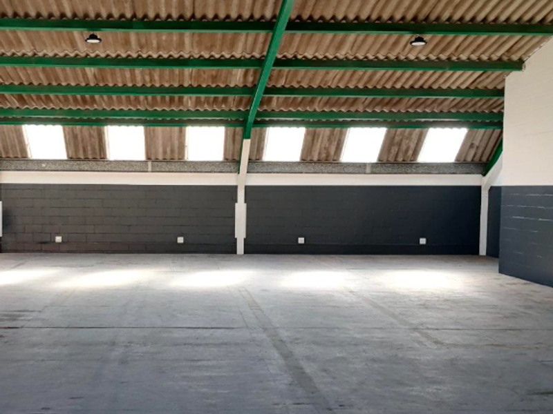 Spacious open-plan office area featuring exposed steel roof trusses, natural light from skylights, and durable concrete flooring with painted block walls.