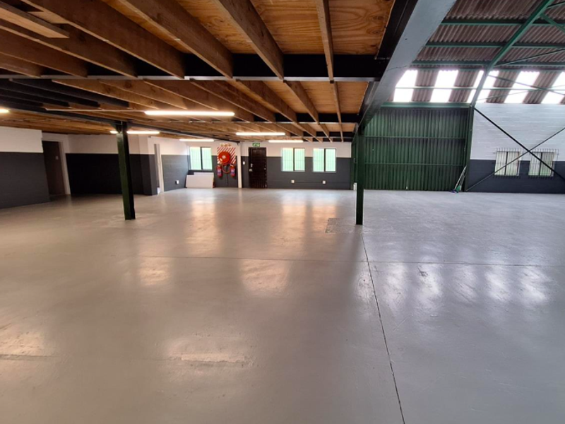 Spacious open-plan office or industrial workspace featuring exposed timber ceiling beams, polished concrete flooring, and high-volume industrial roofing.