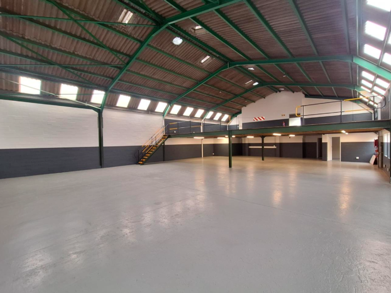 Spacious open-plan office or industrial unit featuring high ceilings with exposed steel trusses, a mezzanine level, and durable epoxy-coated flooring.
