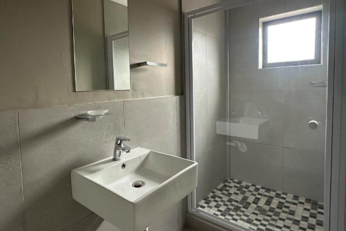 Modern bathroom featuring a wall-mounted basin, chrome fixtures, and a glass-enclosed shower with a decorative tiled floor.
