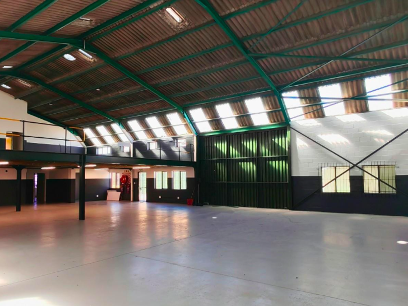 Spacious industrial-style office unit featuring high ceilings with exposed steel trusses, a mezzanine level, abundant natural light from skylights, and durable epoxy flooring.