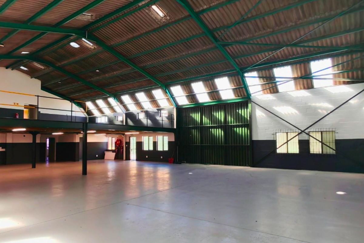 Spacious industrial-style office unit featuring high ceilings with exposed steel trusses, a mezzanine level, abundant natural light from skylights, and durable epoxy flooring.
