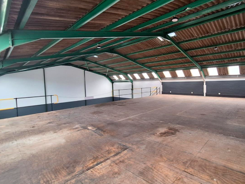 Spacious open-plan mezzanine office area featuring exposed steel roof trusses, industrial lighting, and natural light from skylights, suitable for versatile commercial use.