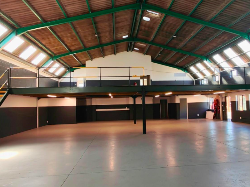 Spacious open-plan office or industrial space featuring a mezzanine level, exposed roof trusses, abundant natural light from skylights, and durable epoxy flooring.