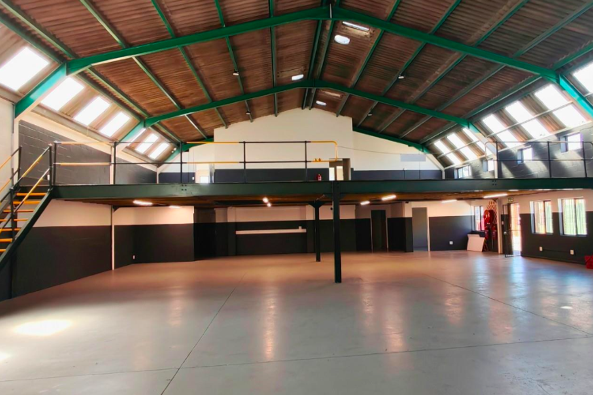 Spacious open-plan office or industrial space featuring a mezzanine level, exposed roof trusses, abundant natural light from skylights, and durable epoxy flooring.