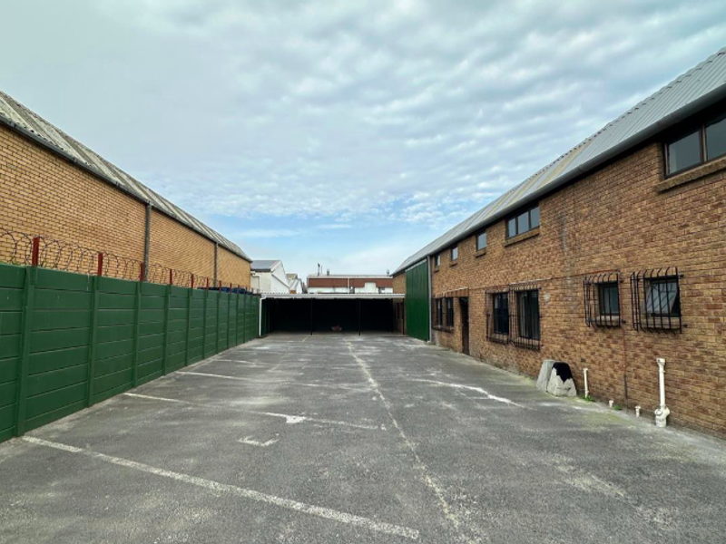 Rear exterior view of the office property featuring a paved parking area, brick building facades, and secure perimeter fencing.