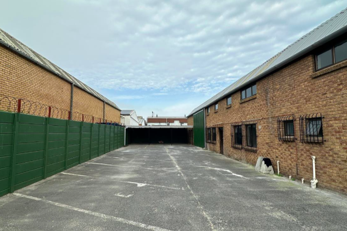 Rear exterior view of the office property featuring a paved parking area, brick building facades, and secure perimeter fencing.