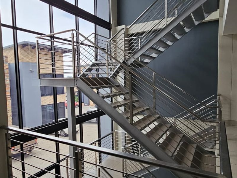 Modern office entrance featuring a striking double-volume glass curtain wall, stainless steel staircase, and contemporary pendant lighting.