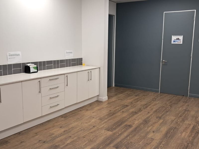 A clean, modern office kitchenette area featuring white built-in cabinetry, a grey tiled backsplash, and wood-look laminate flooring.