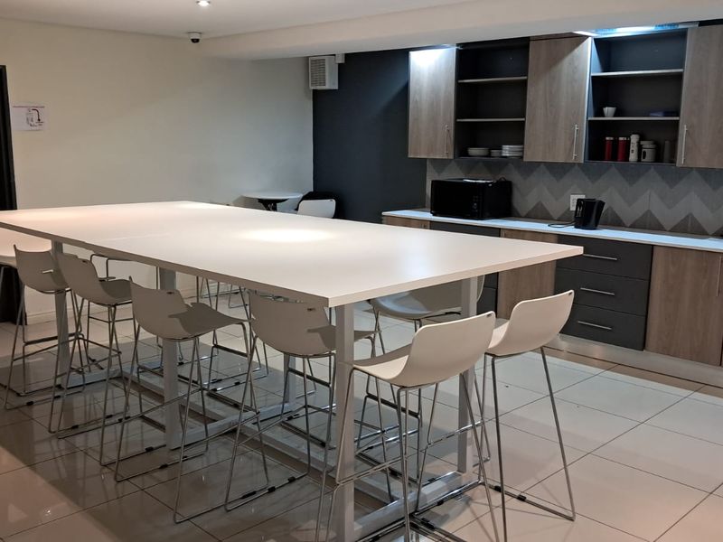 A modern office kitchenette featuring built-in cabinetry, a tiled backsplash, and a large central island with seating, suitable for staff break areas.