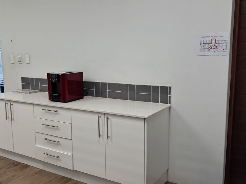 A clean office kitchenette area featuring white built-in cabinetry, a stone countertop, and a modern grey tiled backsplash.