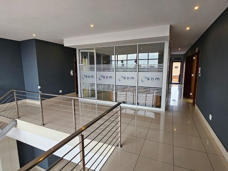Modern office landing area featuring a glass-partitioned office suite, stainless steel balustrades, and polished tile flooring with recessed lighting.