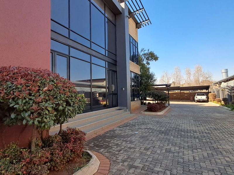Modern office building exterior featuring extensive glass curtain walling, paved driveway access, and secure covered parking facilities.