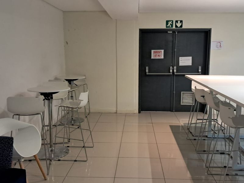 A functional office break-out or communal area featuring tiled flooring and a designated emergency exit door.