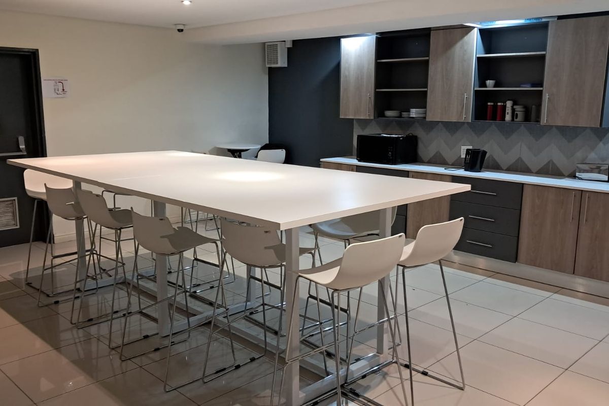 A modern office kitchenette featuring built-in cabinetry, a tiled backsplash, and a large central island with seating, suitable for staff break areas.
