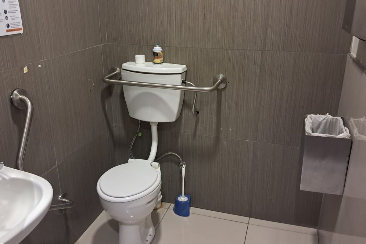 Accessible office bathroom featuring a toilet, washbasin, and stainless steel grab rails with dark wood-look wall tiling.