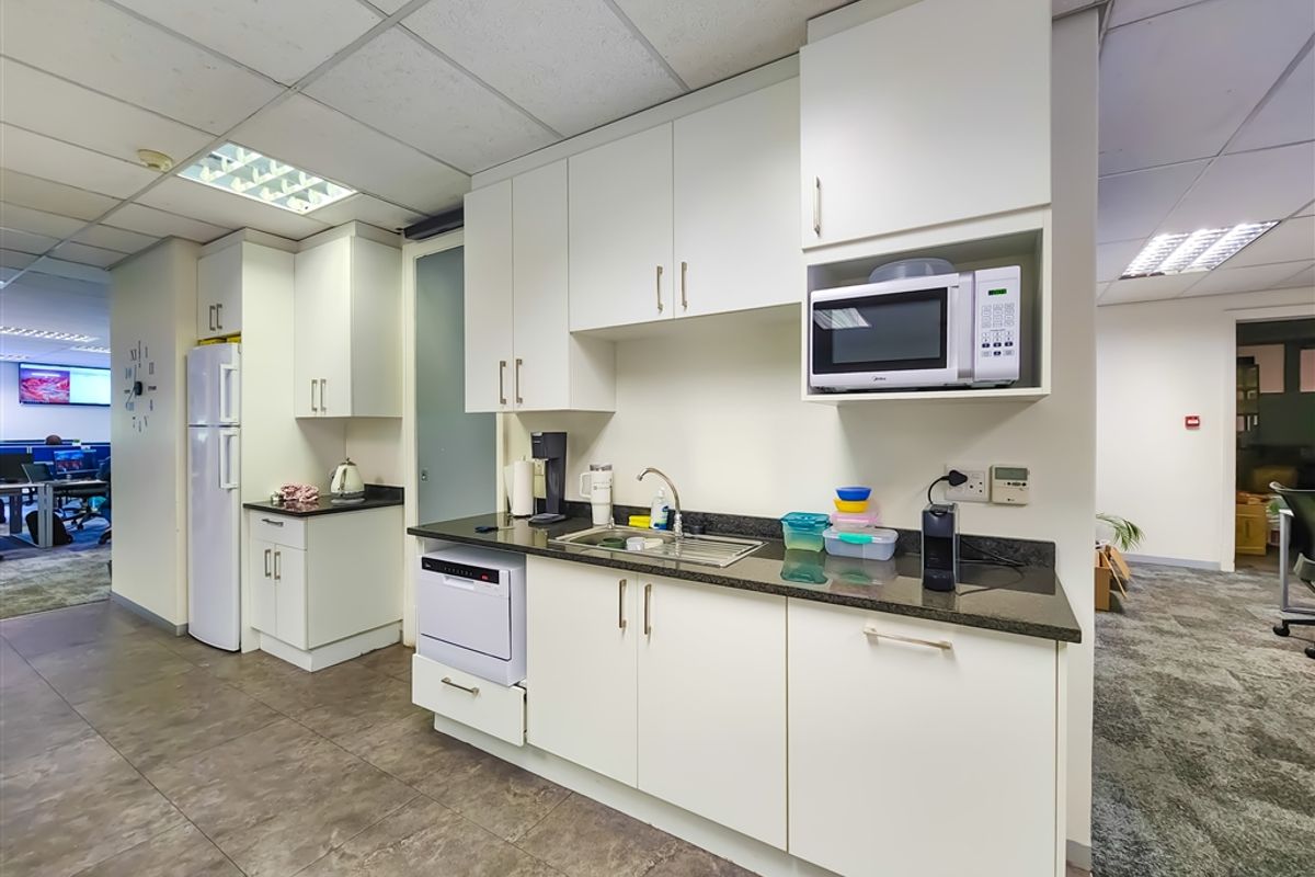 A functional office kitchenette featuring white cabinetry, dark stone countertops, a stainless steel sink, and integrated microwave space.