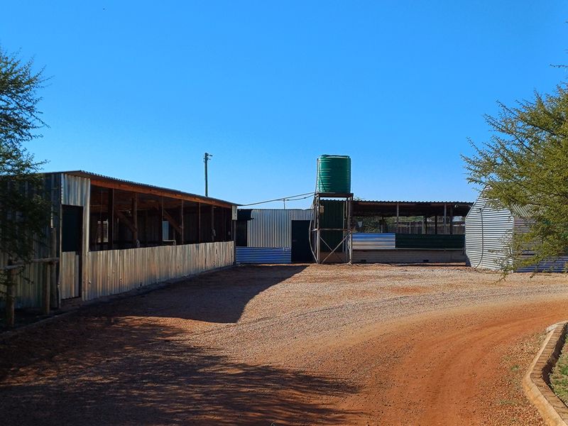 Exterior view of farm outbuildings featuring corrugated iron construction and a raised water storage tank on a dirt access area.