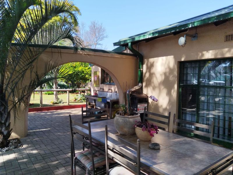 A covered outdoor patio area featuring paved flooring, an arched architectural detail, and a functional utility sink, overlooking the garden.